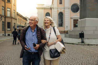 Smiling retired senior couple walking on street in city - MASF40533