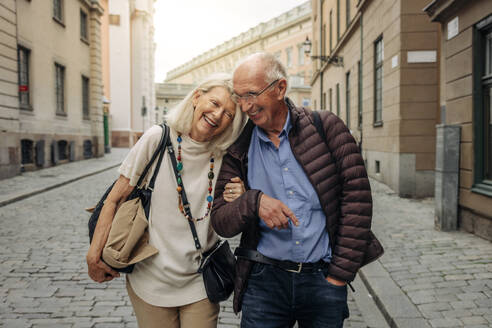 Happy retired senior couple with arm in arm strolling on city street - MASF40536