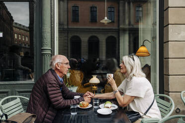 Senior man holding hand of woman while sitting together at sidewalk cafe - MASF40541