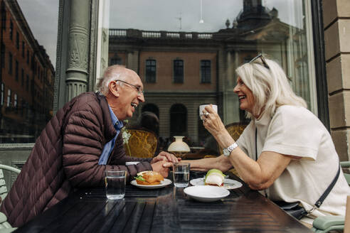 Happy senior man holding hand of woman while sitting together at sidewalk cafe - MASF40543