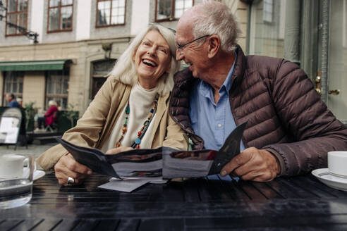 Cheerful senior couple sitting with menu at sidewalk cafe - MASF40545