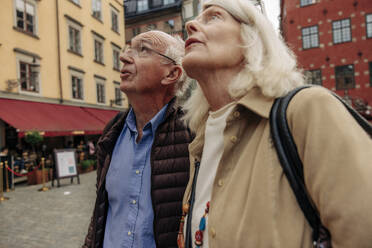 Senior couple looking up while standing together in city - MASF40548