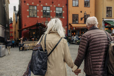 Rear view of senior couple holding hands while walking together in city - MASF40549