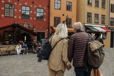 Rear view of senior tourist couple holding hands while walking together in city - MASF40550