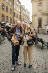Full length of senior tourist couple reading map together in city - MASF40551