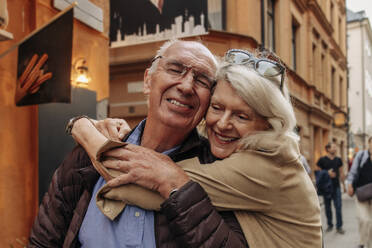Happy senior woman hugging man from behind in city - MASF40555