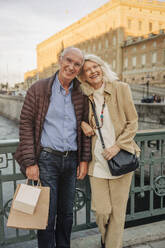 Porträt eines glücklichen älteren Paares, das sich auf ein Geländer in der Stadt stützt - MASF40556
