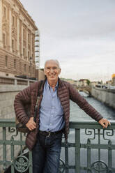 Portrait of smiling senior man leaning on railing over canal - MASF40559