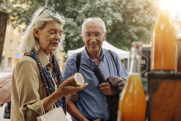 Senior woman examining jar while standing by man at market - MASF40569