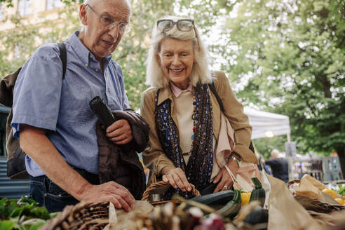 Smiling senior woman and man looking at vegetables on display - MASF40573
