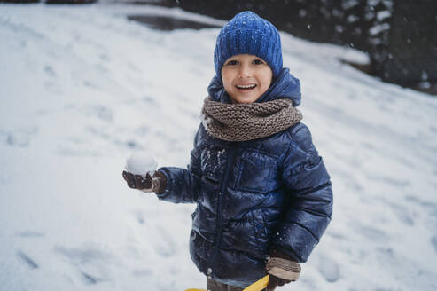 Glücklicher Junge hält Schneeball im Winter - ANAF02379