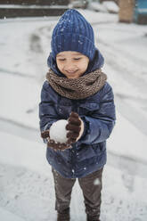 Lächelnder Junge in warmer Kleidung macht Schneeball im Winter - ANAF02393