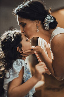 Mother kissing daughter on forehead at home - MFF09437