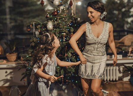 Glückliches Mädchen hält Hände mit Mutter und tanzt in der Nähe von Weihnachtsbaum zu Hause - MFF09438