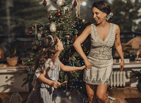 Happy girl holding hands with mother and dancing near Christmas tree at home - MFF09438