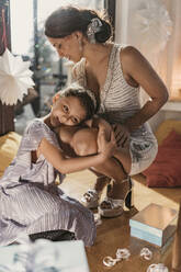 Smiling daughter embracing and leaning on mother's lap near Christmas present at home - MFF09445