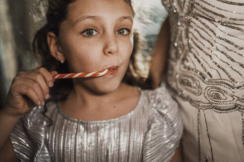 Girl eating candy cane with mother at home - MFF09452