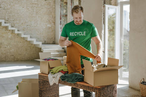 Lächelnde Aktivistin faltet Secondhand-Kleidung in der Nähe der Spendenbox in ihrer Wohnung - YTF01298