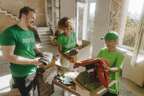 Glückliche Aktivistinnen, die in der Wohnung Kleidung untersuchen und in Kartons verpacken - YTF01310