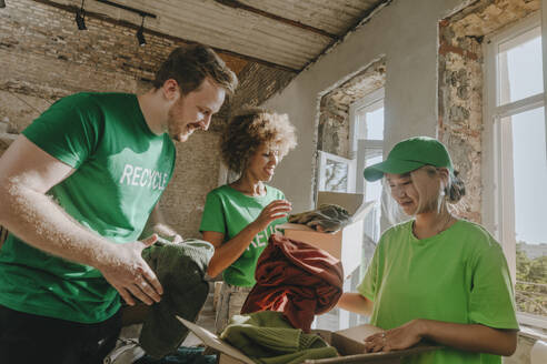 Lächelnde Aktivisten legen Kleidungsstücke in Spendenboxen in einer Wohnung - YTF01311