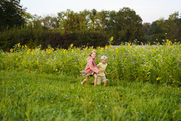 Happy sister and brother running in sunflower field - NJAF00606