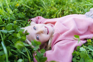 Lächelndes Mädchen mit rosa Sweatshirt im Gras liegend - NJAF00608