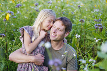 Smiling daughter whispering to father in field - NJAF00614