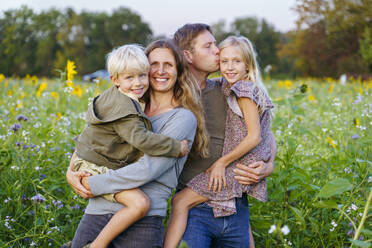 Glückliche Eltern mit Kindern in einem Sonnenblumenfeld - NJAF00615