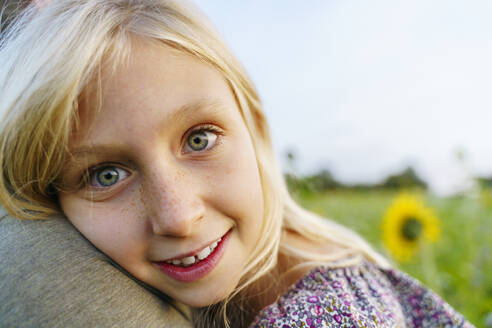 Smiling blond girl leaning on father in field - NJAF00616