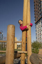 Lächelndes Mädchen spielt auf dem Spielplatz am Klettergerüst - LESF00504