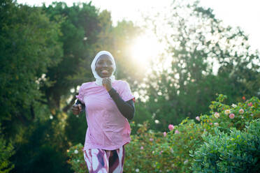 Smiling woman running in park at sunset - GDBF00102