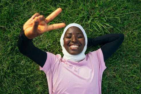 Smiling woman lying on grass and gesturing peace sign - GDBF00105