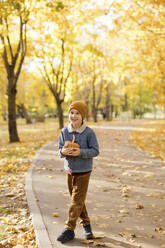 Lächelnder Junge mit Kürbis auf dem Fußweg im Herbstpark - ONAF00665