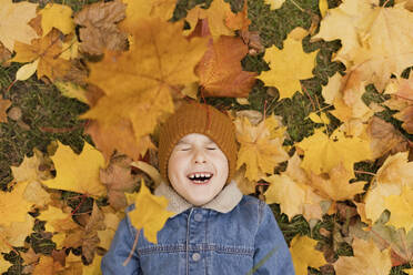 Cheerful boy lying on falling yellow autumn leaves at park - ONAF00671