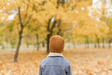Boy wearing denim jacket and yellow knit hat at autumn park - ONAF00673