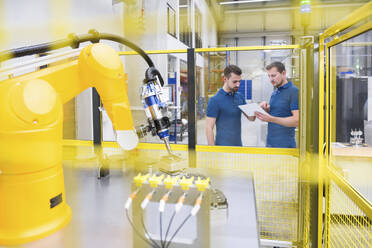 Robotic arm with engineer showing tablet PC to colleague at factory - DIGF20949