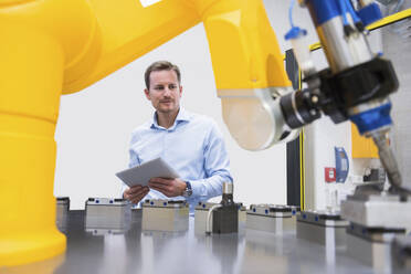 Ingenieur hält einen Tablet-PC und untersucht einen Roboterarm in einer Fabrik - DIGF20951