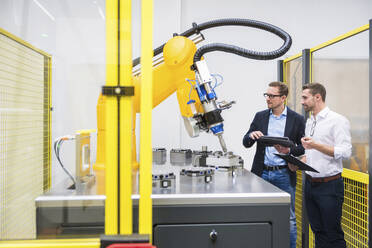 Engineers with tablet PC examining robotic arm in factory - DIGF20952