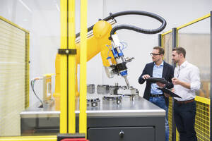 Ingenieure mit Tablet-PC bei der Untersuchung eines Roboterarms in einer Fabrik - DIGF20952