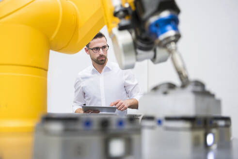 Ingenieur mit Tablet-PC bei der Bedienung eines Roboterarms in einer Fabrik - DIGF20954
