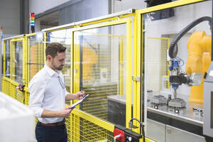 Ingenieur prüft Checkliste in der Nähe eines Roboterarms in einer Fabrik - DIGF20957