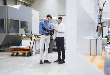 Engineer with file folder discussing with colleague in factory - DIGF20962