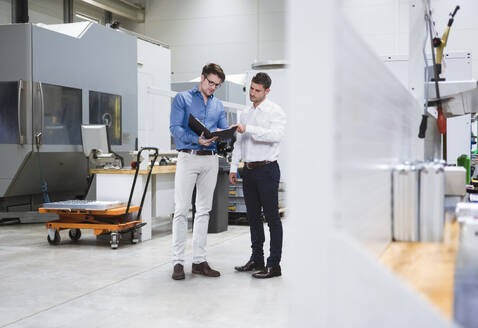 Ingenieur mit Aktenordner bespricht sich mit einem Kollegen in der Fabrik - DIGF20962