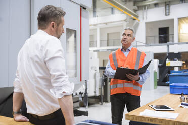 Engineer holding document file and discussing with colleague in factory - DIGF20969