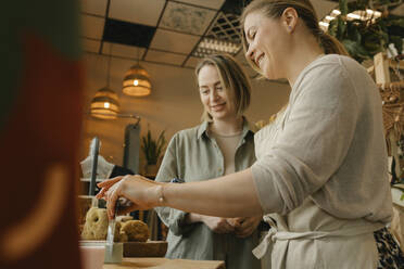 Lächelnde Verkäuferin, die ein Stück Seife von einem Kunden im Geschäft abschneidet - VIVF01152