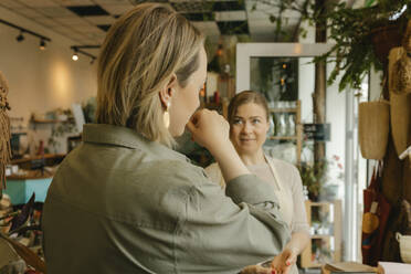 Woman choosing perfume by smelling on hand by owner in store - VIVF01156