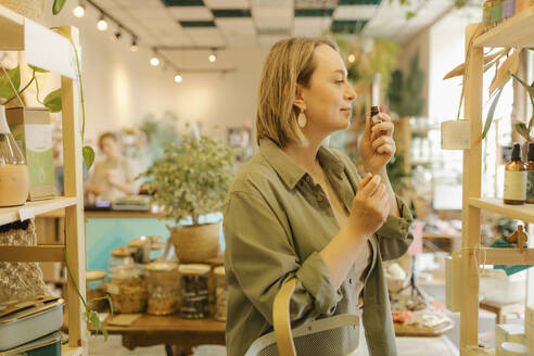 Blond woman smelling oil and shopping in eco-shop - VIVF01178