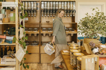 Smiling woman with shopping basket walking around in zero waste store - VIVF01189