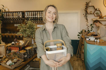 Smiling blond woman holding shopping basket in store - VIVF01220