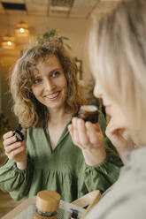 Lächelnde blonde Frau hält Feuchtigkeitscreme für eine Freundin im Laden - VIVF01226